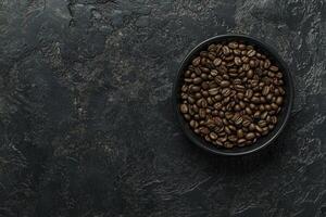 Roasted Coffee Beans in a Black Bowl Against Dark Textured Backdrop photo