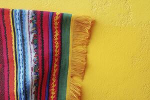 Striped Fringe Textile Hanging on Yellow Wall Texture Backdrop Still Life photo