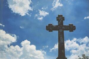 Stone Cross Silhouette Against a Blue Sky with Fluffy White Clouds photo