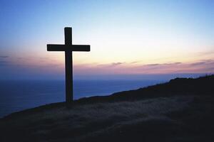 Cross Silhouette on Hilltop at Sunset with Ocean View Background photo