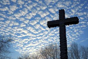 Stone Cross Silhouette Against a Stunning Cloudscape with Trees Below photo