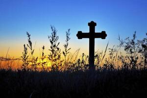 Silhouette of Christian Cross with Sunset Sky and Grasses Background photo