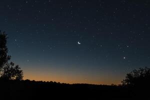 Crescent Moon and Stars Over a Silhouette Landscape at Dusk photo