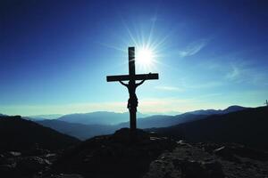 Silhouette of Crucifix on Mountain Peak with Sunburst on Clear Day photo