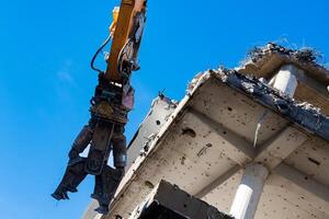 A powerful excavator grips a concrete structure, pulling it apart photo