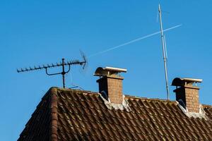 Two chimneys and an antenna stand on a sloped roof against a vibrant photo
