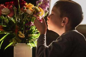 A boy rests his chin on the table, mesmerized by the beauty and scent of the bouquet. photo