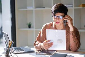 Businesman consulting on phone while using a tablet and reviewing financial documents. photo