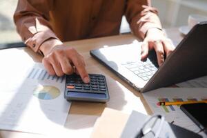 Accountant working on financial calculations using a calculator and laptop for analysis. photo