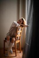 A thoughtful woman sits by the window, dressed in knee-high socks, a shirt, and a sweater photo
