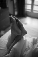 Feet peek out from beneath a soft duvet in a monochrome photograph. photo