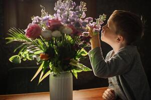 A curious child leans over the table, his nose almost touching the fragrant blossoms. photo