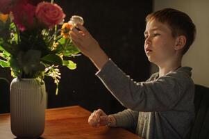 Sitting at the table, a boy gently explores a bouquet, lost in its fragrance. photo