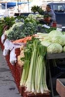 A stand is packed with organic vegetables, with a towering leek standing out among zucchini, potatoes, and beets. photo