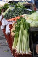 Shoppers browse baskets filled with fresh vegetables, while a child curiously points at a massive leek among the greens. photo