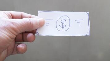 A piece of paper resembling a dollar bill, with a dollar sign drawn in the center, is being held in hand. This item may be used for illustration or as a humorous element. photo