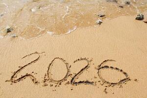 words 2026 and number written in sand on beach with waves on top. Happy New Year background photo