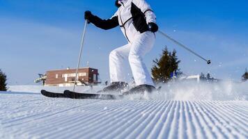 A skilled skier, dressed in a stylish white jacket and pants, expertly navigates down a beautifully groomed slope on a sunny winter day, carving turns and sending snow flying in every direction. photo