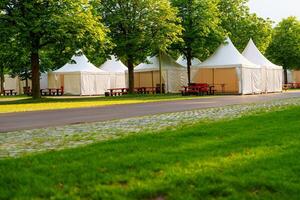 Several white party tents are set up in a park with green trees and a lawn. The tents are surrounded by trees and grass, creating a beautiful and natural setting. photo