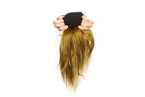 A hand is gripping a handful of blond hair, pulling it through a torn hole in a solid white surface. Only the hand and hair are visible, creating a striking contrast against the white background. photo