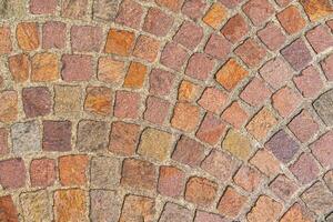 The image features a red cobblestone street pavement texture. Each stone varies in shade and showcases a classic herringbone pattern, giving it an old and weathered charm. photo