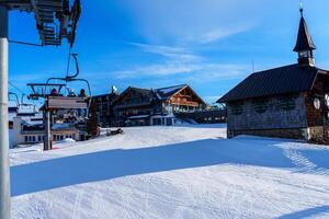 The ski resort is beautifully covered in a thick blanket of snow, with majestic trees lining both sides of the charming building. At the top, a classic clock tower adds a touch of elegance. photo