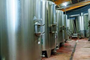 A row of large stainless steel fermentation tanks in a modern winery facility. These tanks are essential for storing, fermenting, and producing high-quality wine to meet consumer demand. photo