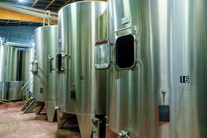 A row of six large stainless steel fermentation tanks in a modern winery. These tanks are essential for the fermentation process, allowing winemakers to create high-quality wines with precision. photo