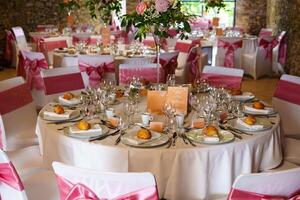 This elegant wedding reception table showcases a white tablecloth adorned with a pink and white floral centerpiece, complemented by pink napkins and matching dinnerware. photo