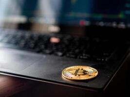 A gold coin with the Bitcoin on it is sitting on a laptop keyboard photo