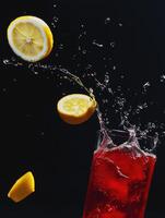 A glass of red liquid with a lemon slice in it is splashing water photo