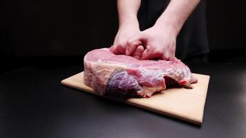 Male hands massaging a large beef steak on a black background. Preparing a tender beef steak for baking. Demonstration of the effect of massage on the body using a piece of meat as an example video