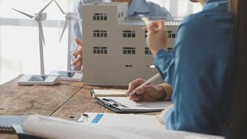 A woman is writing on a notepad while looking at a model of a wind turbine video
