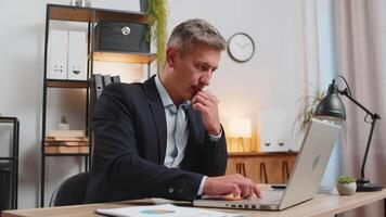 Young businessman using laptop while thinking about important creative project decision at desk video