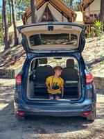 Boy having fun while sitting in trunk near glamping campsite photo