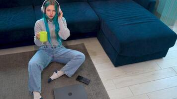 High angle shot of a beautiful blue haired hipster working from home sitting, in a break time listening to music with headphones and taking a selfie. Using technology, working at home. video