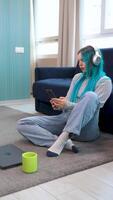 Vertical footage of a beautiful blue-haired hipster working from home sitting, in a break moment listening to music with headphones and taking a selfie. Using technology, working at home. video