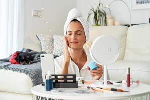 Female applying cream on face while recording on smartphon photo