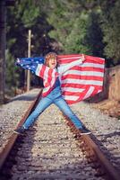 Joyful boy standing with USA flag on rails of railway photo