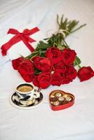 Bouquet of red roses and cup of coffee on bed photo