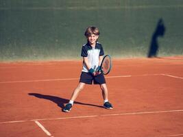 Happy child smiling while practicing tennis on clay court photo