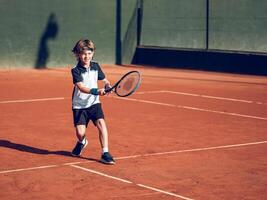 Adorable little boy running to hit ball while playing tennis photo
