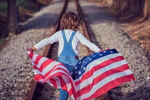 Kid holding USA flag while walking on rails photo