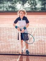 Smiling kid standing near net on court after playing tennis photo