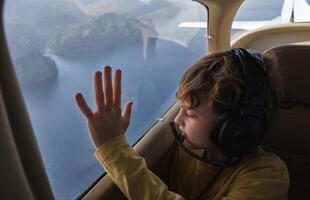 Curious boy looking out airplane window flying above sea photo