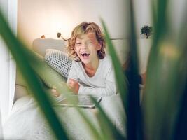 Excited boy lying on sofa watching on tablet photo