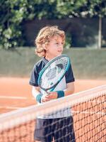 Cute boy tennis player standing near net with racket on court photo