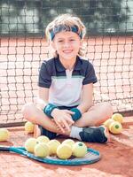 Content kid tennis player resting on court and smiling after mat photo