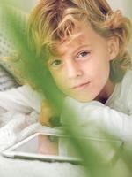 Charming preteen boy lying with tablet and looking at camera photo