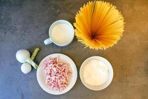 Raw spaghetti with bacon slices and milk cream in cup photo